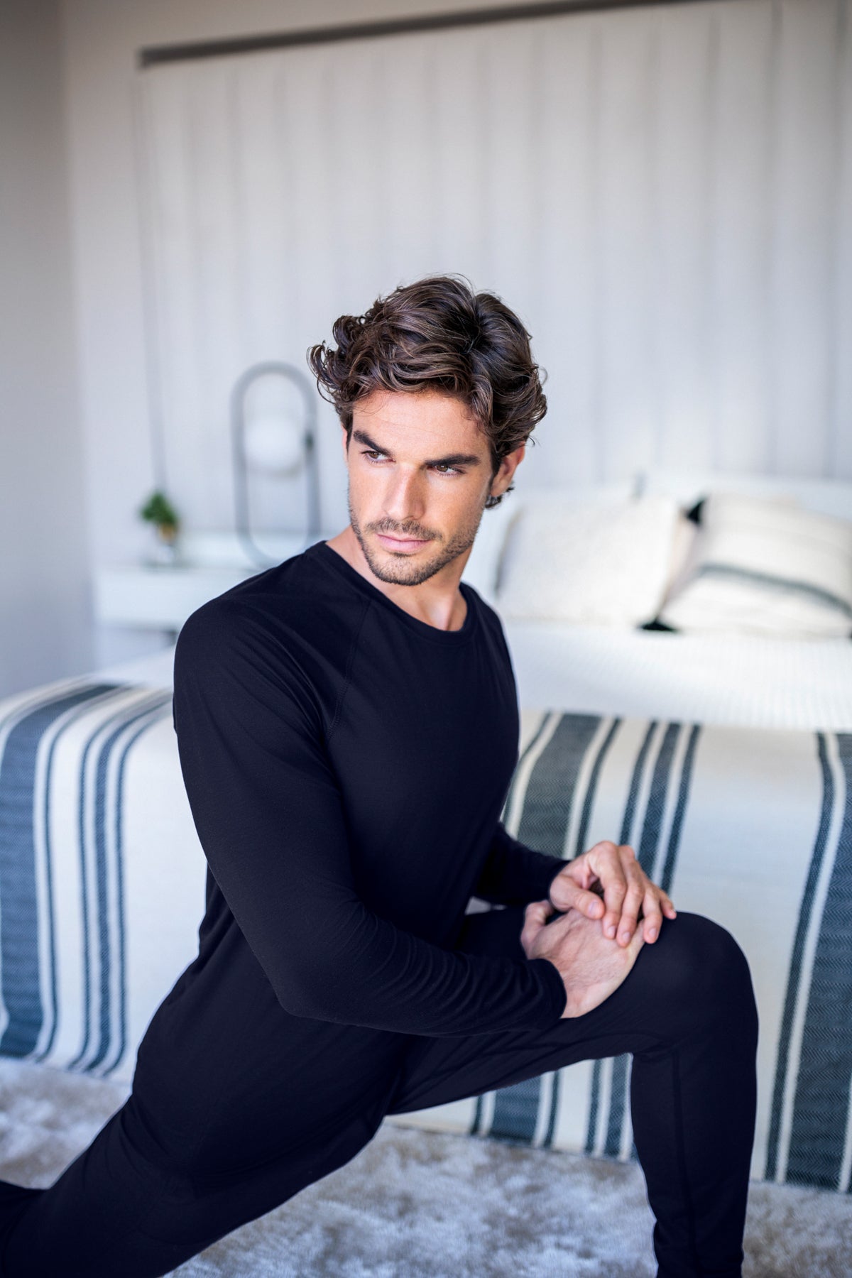 Mann i temperaturregulerende restitusjonstrøye som sitter på seng – utviklet for bedre søvn og raskere restitusjon etter trening